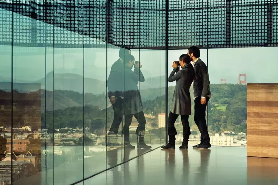 Two people peer through glass walls at the de Young Museum in San Francisco.