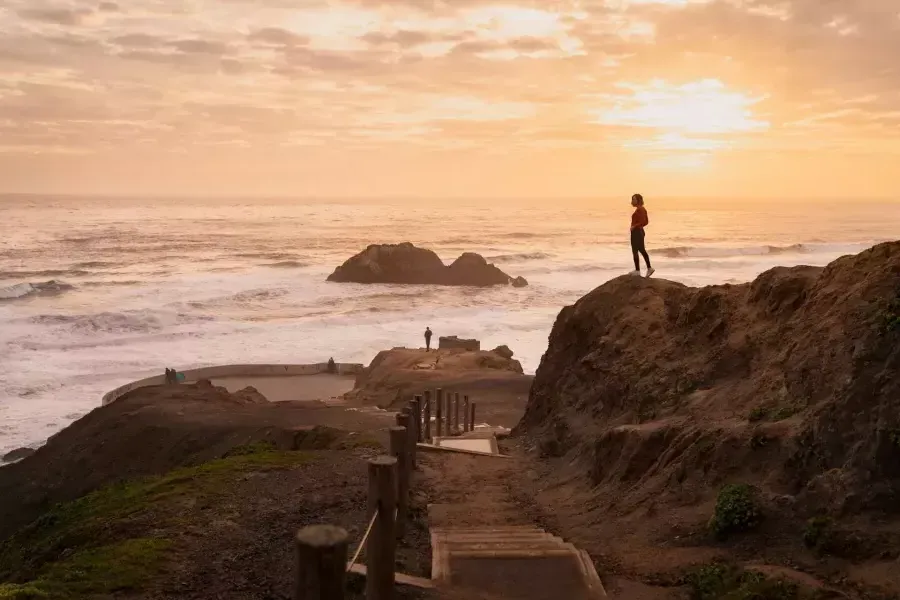 Two people stand on rocks overlooking the ocean at Sutro Baths in San Francisco.