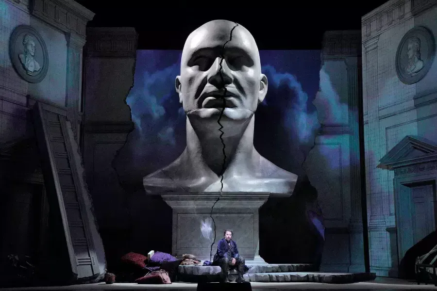 A giant bust of a man looms over two actors on stage in a production of Don Giovanni 在贝博体彩app.