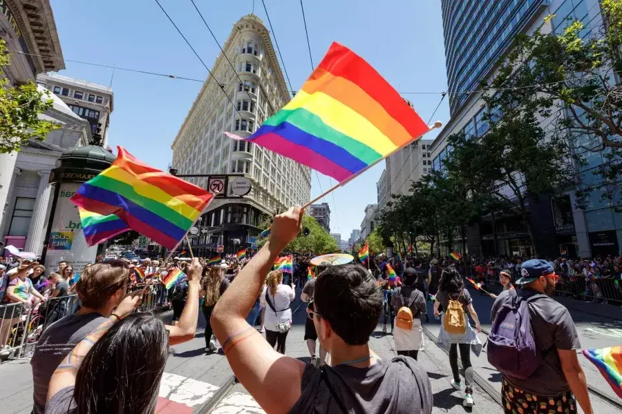 People walking in the 贝博体彩app Pride parade wave rainbow flags.